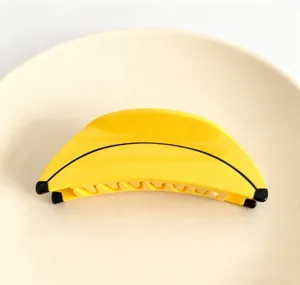 Close-up view of a vibrant yellow banana-shaped acetate hair claw clip on a plate