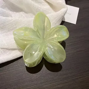 Close-up detail of light green plumeria-shaped resin hair claw clip on dark wood surface