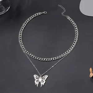 Close-up detail of double-layered silver necklace with cuban chain and butterfly pendant