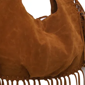 Macro view showing the soft brown suede texture and decorative tassels of the hobo bag