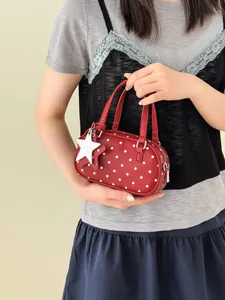 Red polka dot bowling style handbag with a white star charm accessory held by a model.