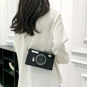 Unique black glittery camera-shaped box bag shown worn as a stylish crossbody bag