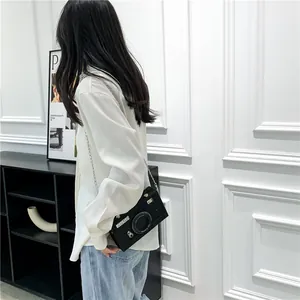 Side view detail of a stylish camera-shaped crossbody box bag worn by a female model