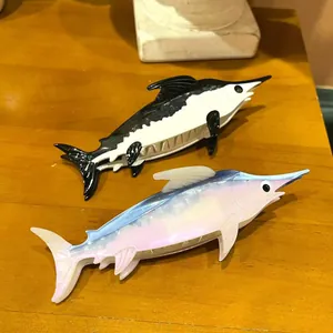 Detail view of two ocean-themed acetate marlin hair claws on wood surface.