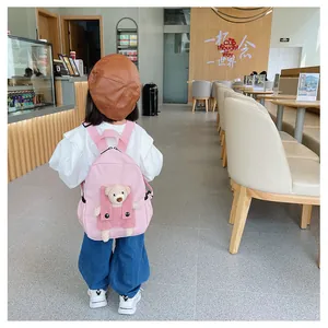 Sac à dos rose pour enfant avec un ours en peluche, porté par un enfant dans un café.