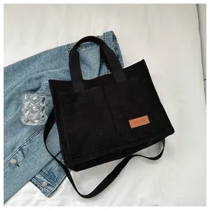 Close-up view of a black corduroy large capacity tote bag featuring a FASHION leather patch