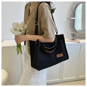 Black corduroy large capacity tote bag worn by a model in a stylish indoor setting