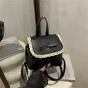Close-up detail of black oily leather backpack with white lace trim and decorative bow.