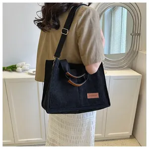 Side view of a large black corduroy tote bag with stylish brown handles and a long strap.
