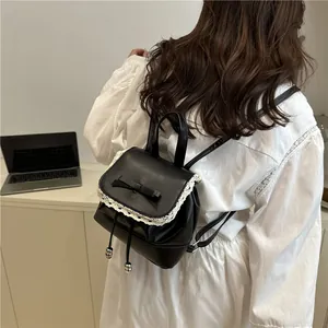 Detail of a black faux leather mini backpack with lace trim and bow on a model's back.