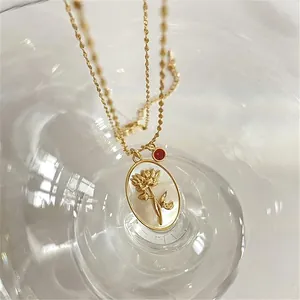 Macro detail of a gold oval pendant featuring embossed flower and a small red gemstone