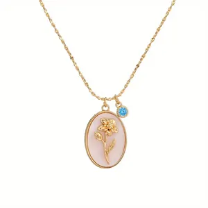 Close-up of gold floral oval pendant necklace with a blue gemstone charm detail.