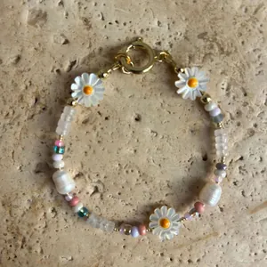 Détail d'un bracelet fait main avec marguerites et perles baroques sur fond de pierre