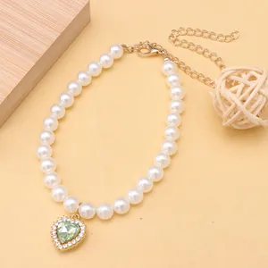 Detail shot of pet pearl necklace with a sparkling green heart pendant and gold chain