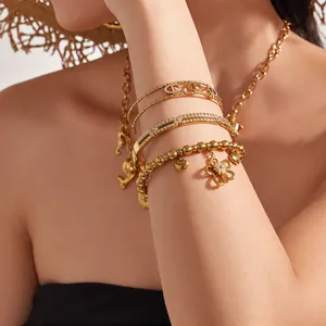 Close-up of gold-plated flower and pig nose charm bracelets on model wrist
