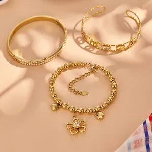 Set of three elegant gold-plated jewelry pieces including flower charm bracelet and bangles
