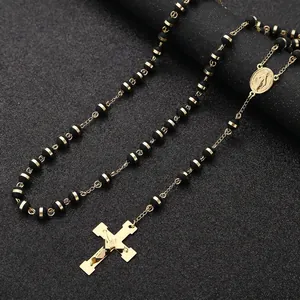 Detailed view of a stainless steel rosary necklace with matte black beads and gold crucifix.