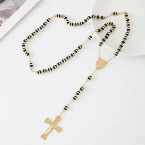 Macro detail of a stainless steel rosary necklace with gold-toned cross and black beads