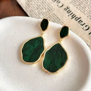 Vintage irregular green emerald drop earrings with gold plated edges on a ceramic plate