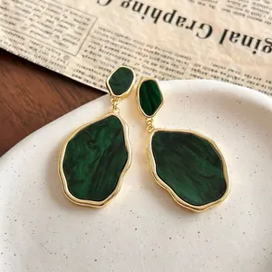 Close-up of vintage irregular green earrings with marble texture on ceramic plate
