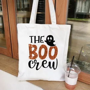 Detail shot of white canvas tote bag with orange glittery Boo Crew Halloween graphic.