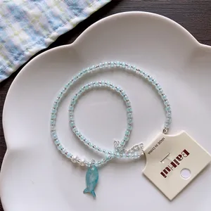 Detail view of summer island beaded necklace with a blue fish pendant on a white plate.