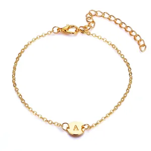 Detail view of a gold chain bracelet featuring an engraved letter A on a round charm.