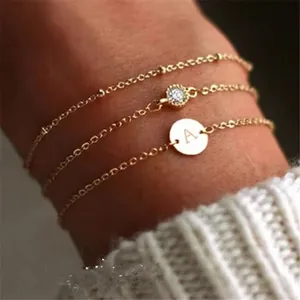 Layered gold initial bracelet set with engraved letter A round disc and crystal charm.