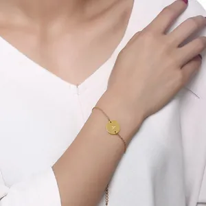 Detailed shot of a delicate gold-finish chain bracelet featuring a round disc engraved with the letter A.