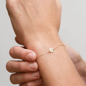 Close-up of a delicate gold chain bracelet featuring a round disc engraved with the letter K.