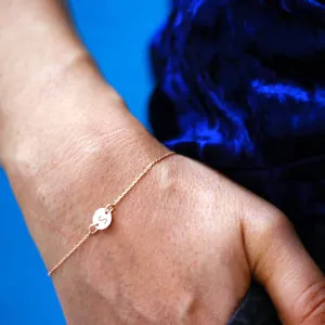 Detailed view of a gold initial bracelet with an engraved letter S on a round charm.