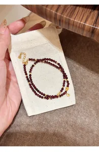 Detailed macro shot of natural garnet double-wrap bracelet on a cream linen jewelry pouch