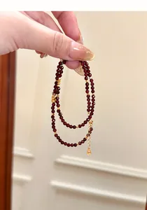 Detailed hand-held view of a double-layer natural garnet stone bracelet with gold charms.