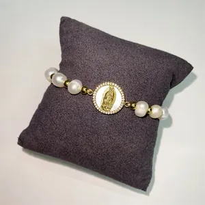 Detail view of handmade pearl bracelet with Virgin Mary shell charm on display pillow