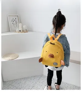 Een peuter met een schattige gele kuiken rugzak in een minimalistische witte kamer.