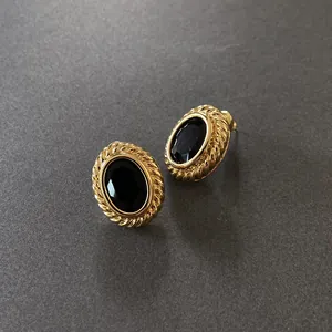 Close-up of French vintage gold earrings with oval black gemstones and rope texture