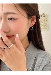 Close-up of sparkling lightning bolt drop earrings and minimalist rings on a model
