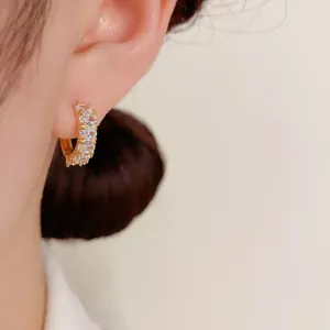Close-up of a dainty gold-plated hoop earring with sparkling cubic zirconia on a model's ear