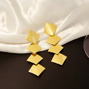 Gros plan de boucles d'oreilles pendantes géométriques dorées sur satin blanc élégant.