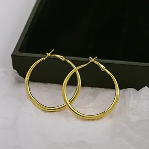 Gros plan de grandes boucles d'oreilles créoles plaquées or sur papier blanc texturé