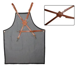Vue détaillée des sangles croisées en cuir marron réglables sur un tablier de travail en denim.