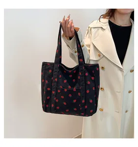 Black corduroy strawberry pattern tote bag held by a person wearing a white trench coat