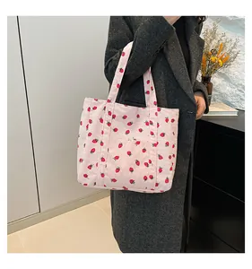 Close-up detail of pink strawberry print corduroy tote bag held by model in a grey coat