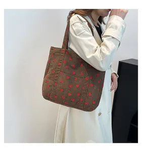 Detailed shot of dark brown corduroy tote bag with red strawberry pattern embroidery.