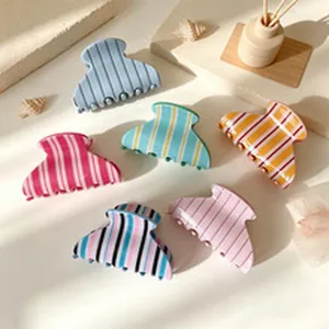 Detailed view of six colorful vertical striped hair claw clips on a cream surface
