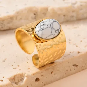 Detail of gold stainless steel ring with oval white stone and hammered texture.
