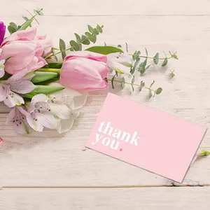 Detail of a pink thank you card with white text on a light wood background with flowers