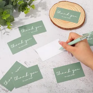 Close-up showing a hand writing on the blank back of a sage green thank you card.