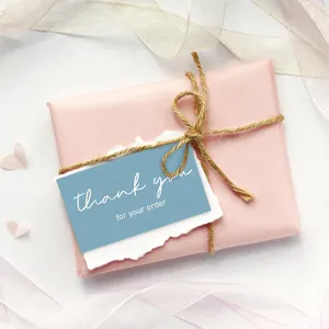 Close-up detail of a blue thank you for your order card on a pink gift wrap with rustic twine