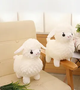 Two fluffy white plush sheep toy dolls sitting on a cozy beige upholstered chair